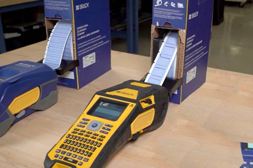 Una gran caja de etiquetas que se alimentan de forma continua hacia el interior de una impresora de etiquetas M610.