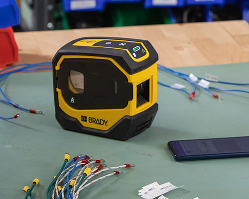 La impresora M511 con cables etiquetados y un teléfono móvil.